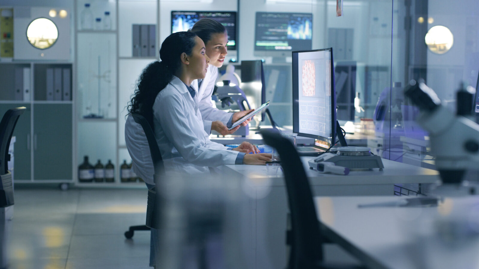 Focused, serious medical scientists analyzing research scans on a computer, working late in the laboratory. Lab workers examine and talk about results from a checkup while working overtime