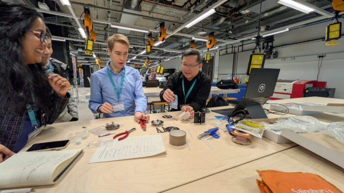Image from the workshop 'Knowledge of the Nanoscale: Developing AFM Activities for Outreach' showing three people clustered around a table examining scientific equipment.